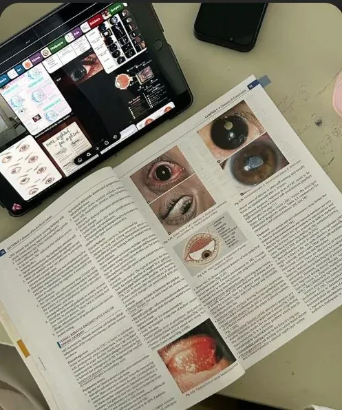 Livro de oftalmologia aberto com imagens clínicas, ao lado de um tablet com anotações